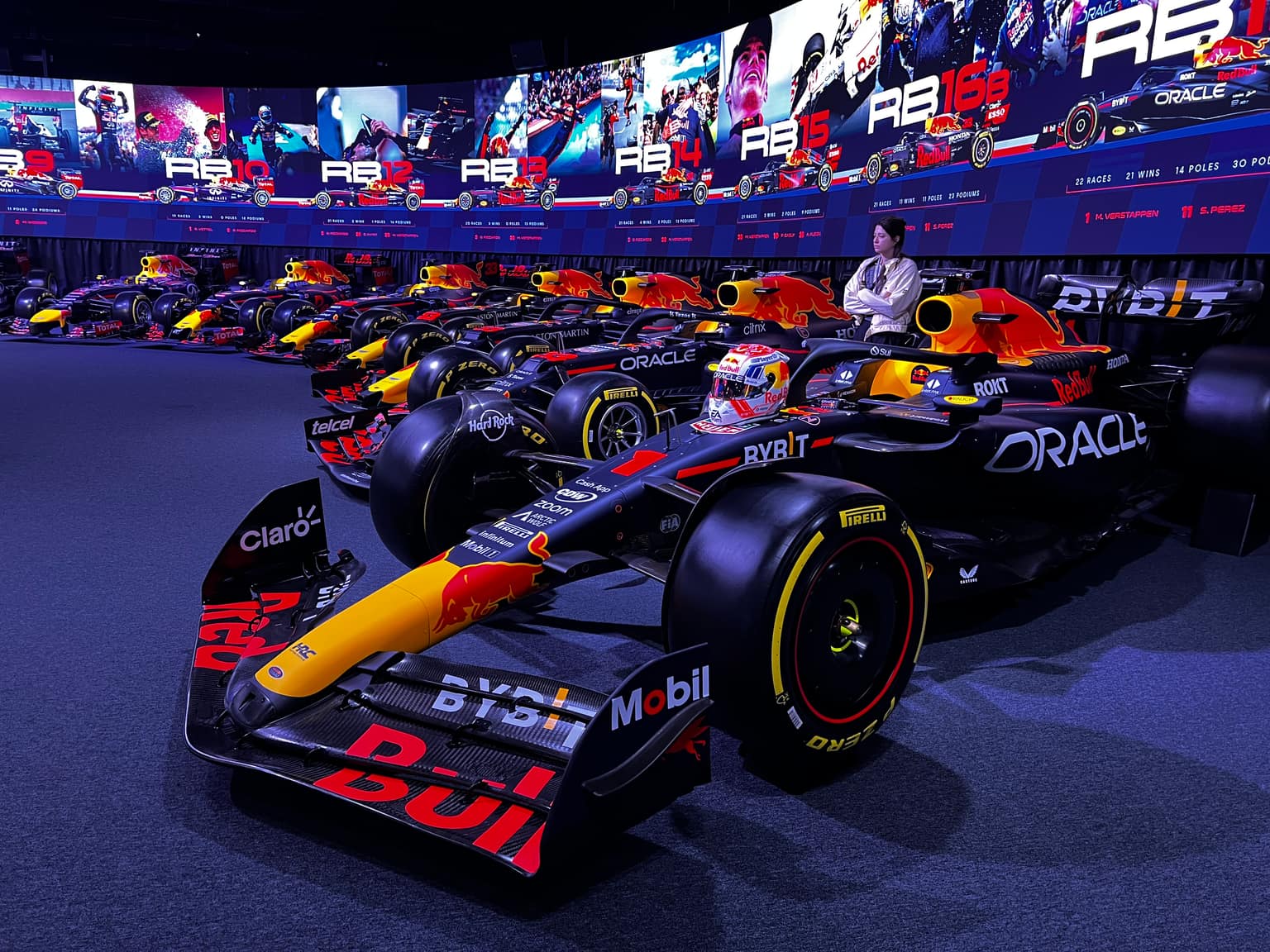 Dark gallery with a sweeping row of Oracle Red Bull Racing F1 cars and a curved LED wall showing model years, driver portraits, and season statistics